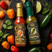 Two bottles of Pepper Palace hot sauce, King Habanero and King Jalapeño, arranged on a dark textured surface with fresh peppers, cilantro, and lime wedges.