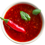 A bowl filled with hot sauce and a garnish of a pepper and leaves